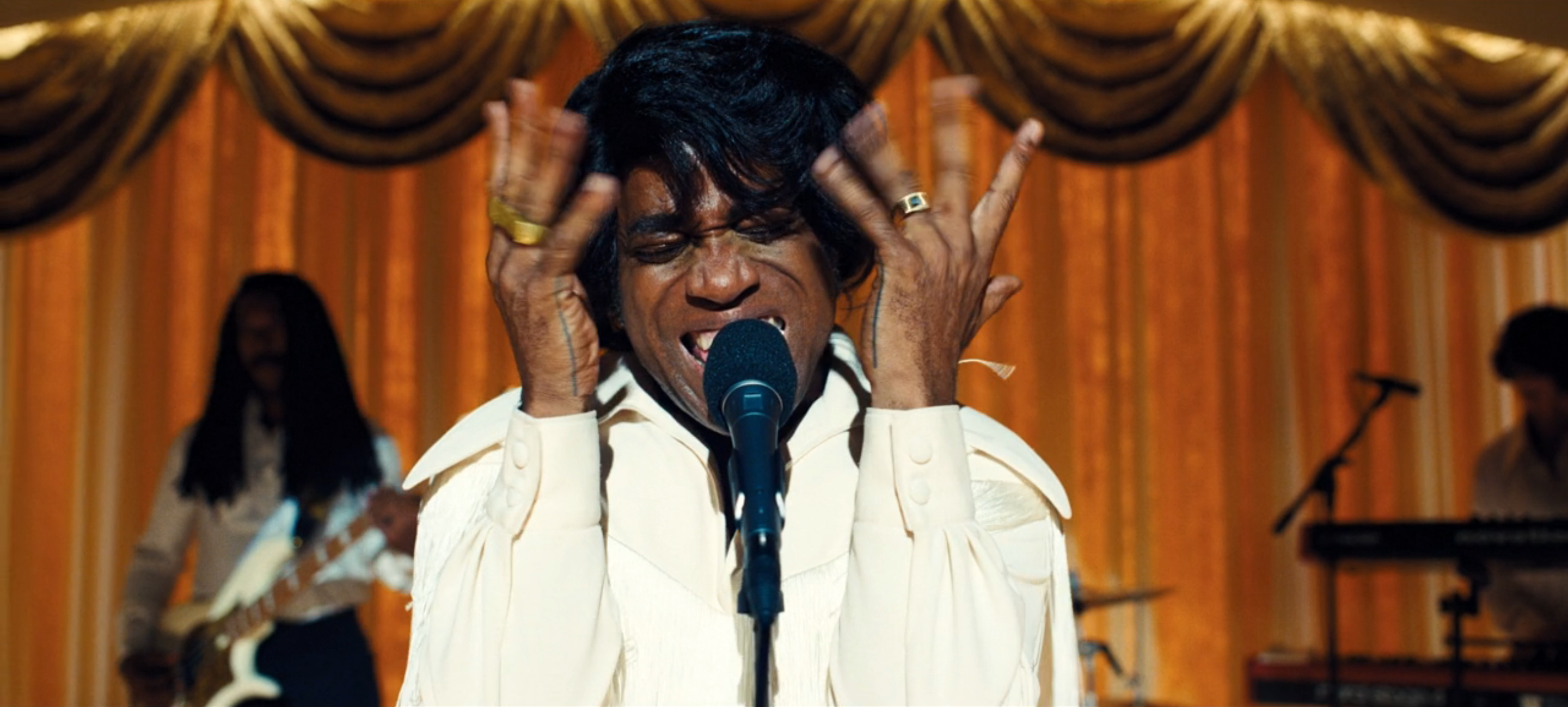 Musical performance with a vocalist gesturing at a microphone.
