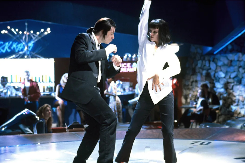 Two people dancing energetically in a club setting, wearing retro-style clothing