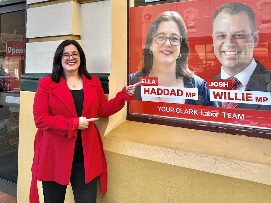 A woman points to a poster of herself in a window.
