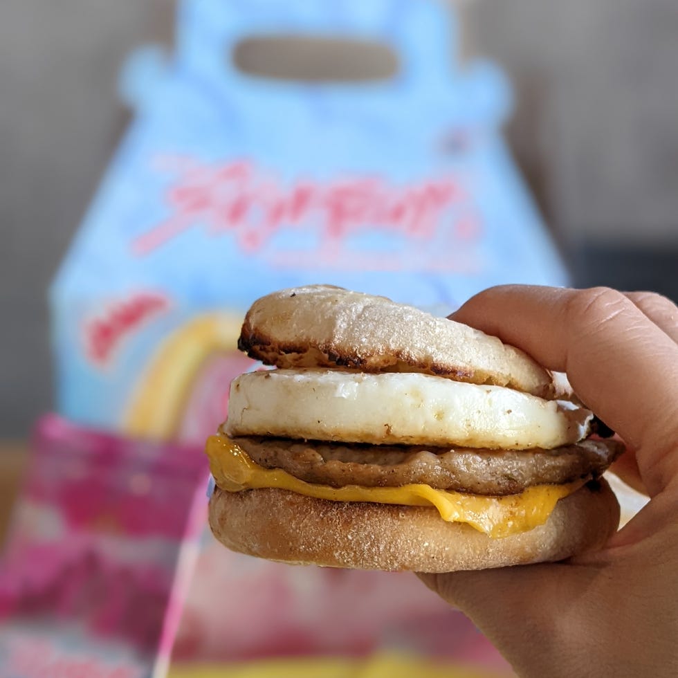 Breakfast sandwich held in hand with colorful packaging in the background. Breakfast sandwich held in hand with colorful packaging in the background.