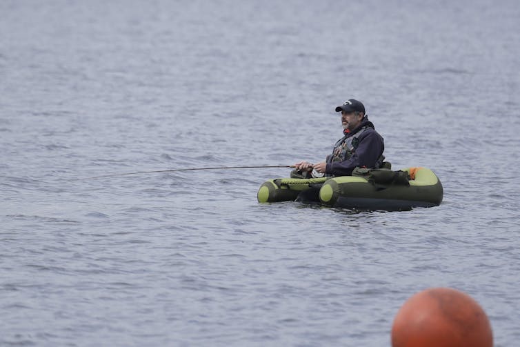 A person holding a fishing rod uses a float to remain above the surface of a body of water.