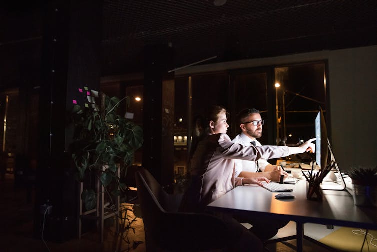 A man and a woman looking at a taptop in a darkened office at night