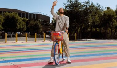 Steph Curry waving  on a rainbow bike in a street paved with rainbow lines.