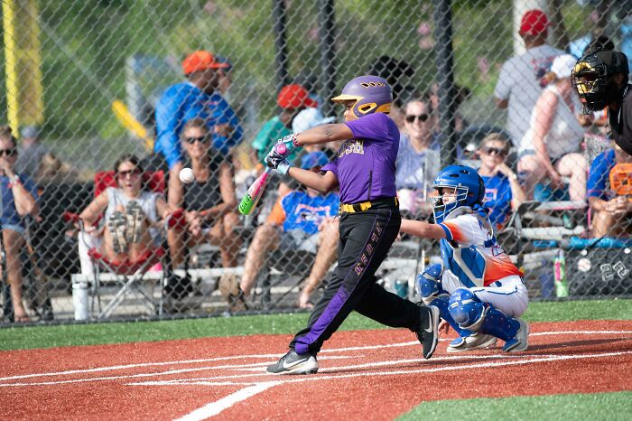 Child playing baseball swinging bat while catcher and spectators watch during youth sports game.