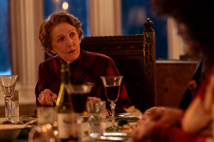 Patricia Hodge as Miriam Crace in Marble Hall Murders, at a dinner table with wine glasses on it, looking at the person next to her.