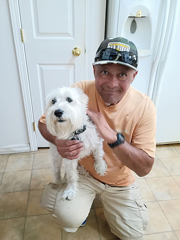 Mark Montoya kneeling with his white dog, Sammy.