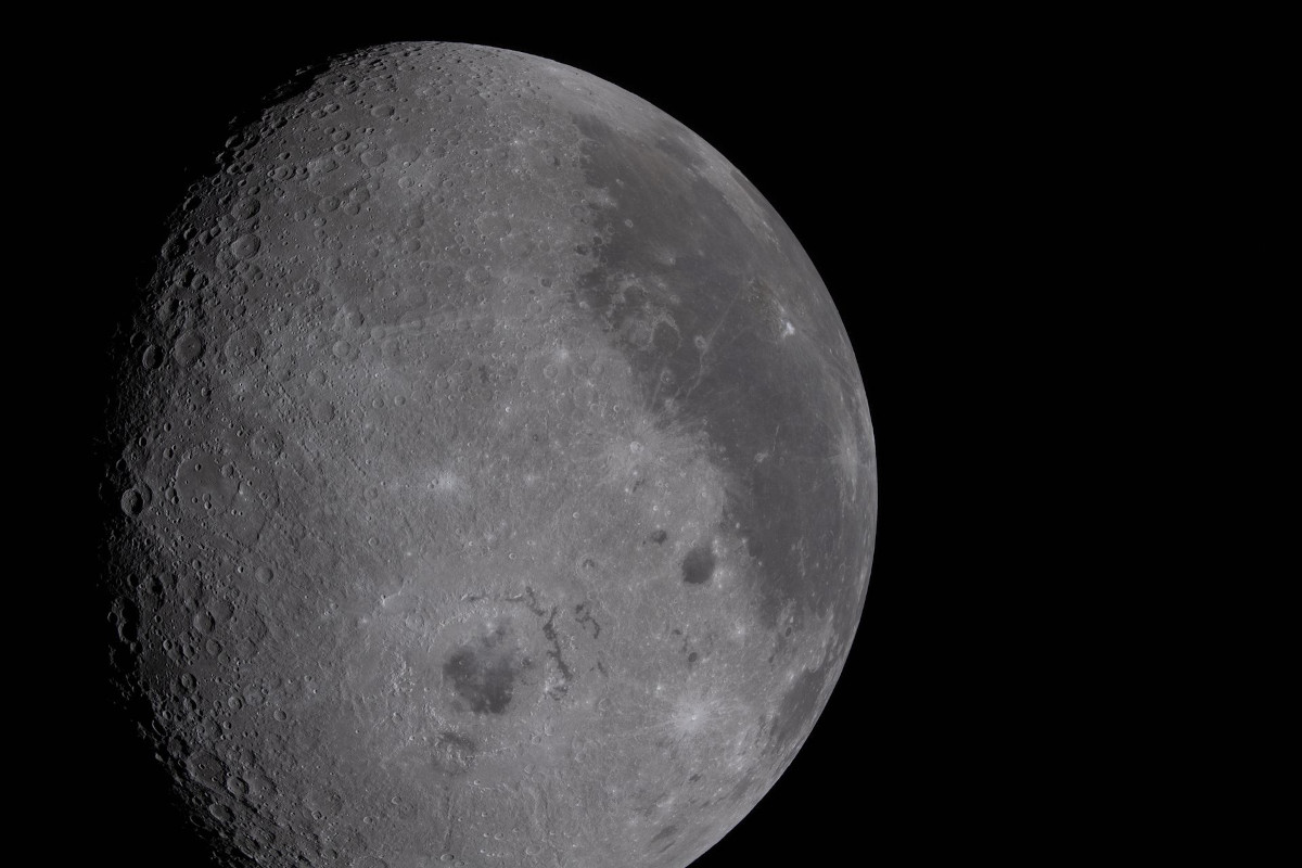 A wide picture of the moon, showing a grey landscape filled with craters and a darker grey patch to the right of the moon.