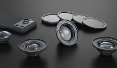 Four camera lenses, three round lens filters, and a smartphone with a textured back are arranged on a dark surface, showcasing photography accessories in a neat layout.