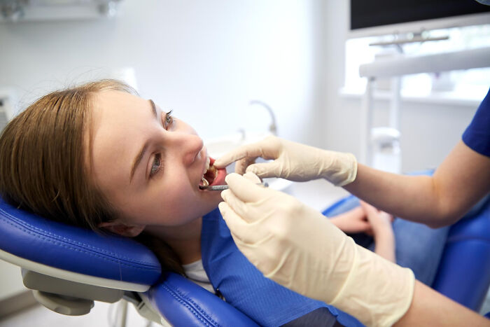 Patient in dental chair receiving oral examination from surgical staff wearing gloves in a clinical setting under sedation