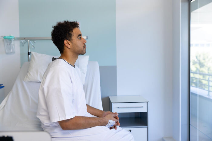 Patient sitting in hospital gown looking out window, illustrating surgical staff stories of unhinged patient confessions under sedation