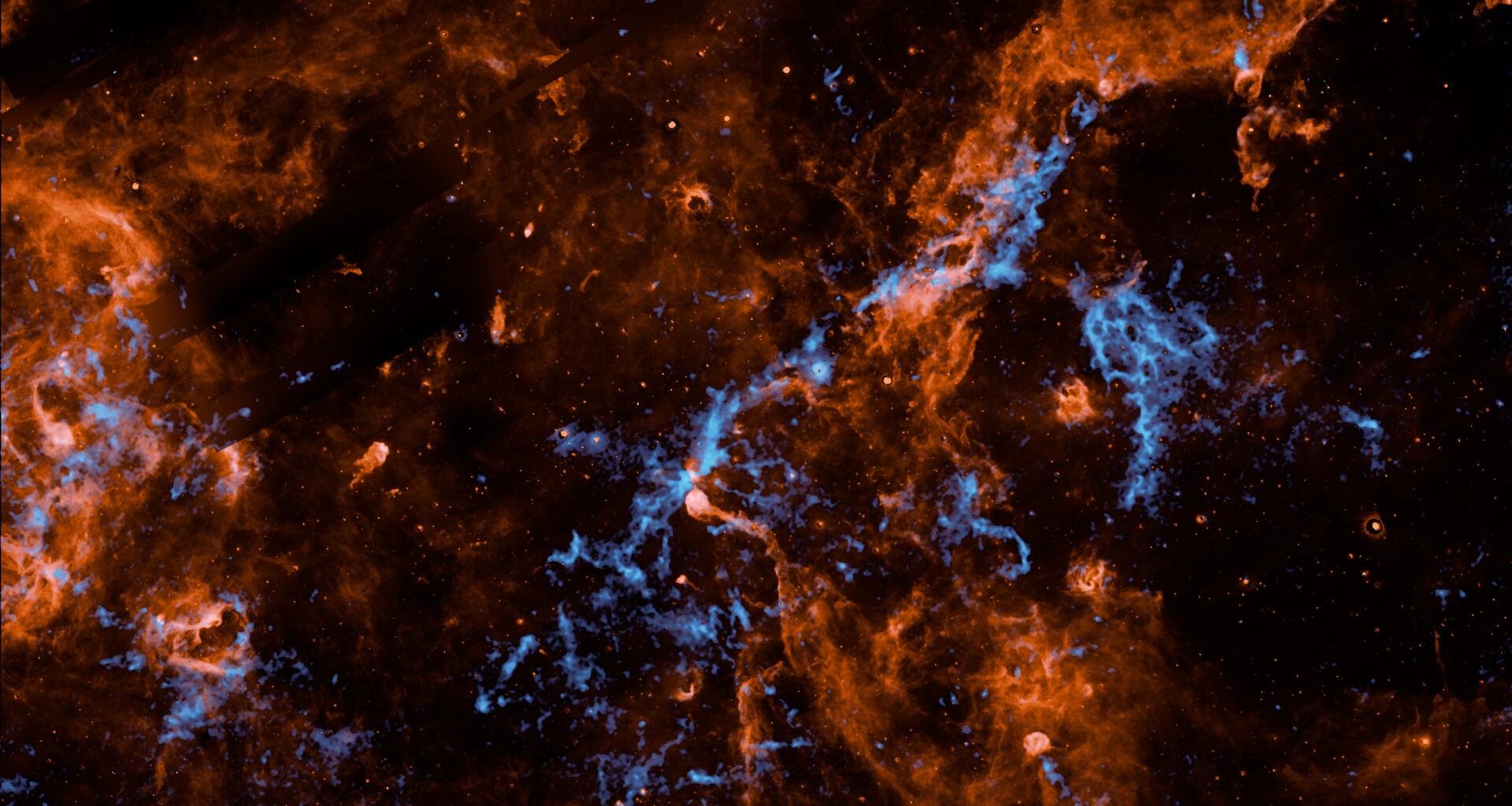 Wispy filaments of vibrant orange and electric blue cosmic dust and gas weave through a dark, star-studded expanse of outer space, creating a chaotic and intricate web of celestial matter.