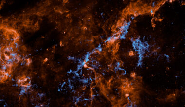 Wispy filaments of vibrant orange and electric blue cosmic dust and gas weave through a dark, star-studded expanse of outer space, creating a chaotic and intricate web of celestial matter.