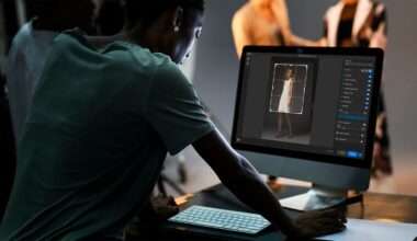 A person uses a desktop computer to edit a photo of a woman in a white dress; other people and studio lighting equipment are visible in the blurred background.