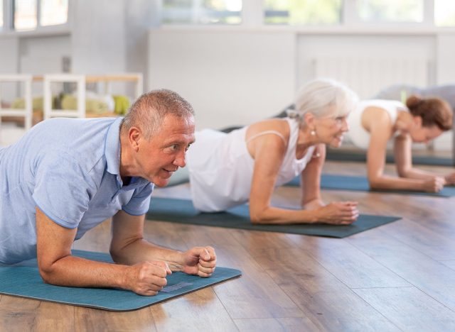 Active pensioners in sportswear performing plank exercise during group Pilates workout in fitness studio