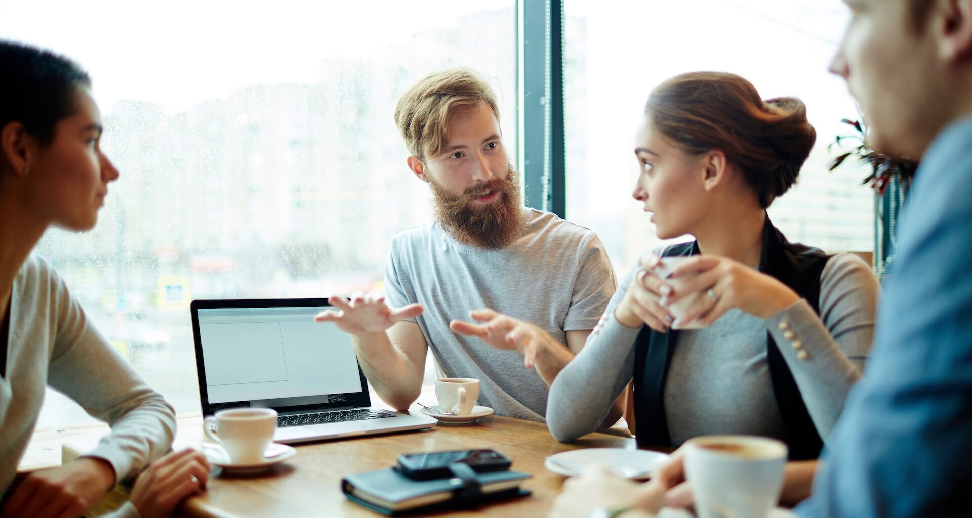Four people in a relaxed business meeting discussing information on a screen