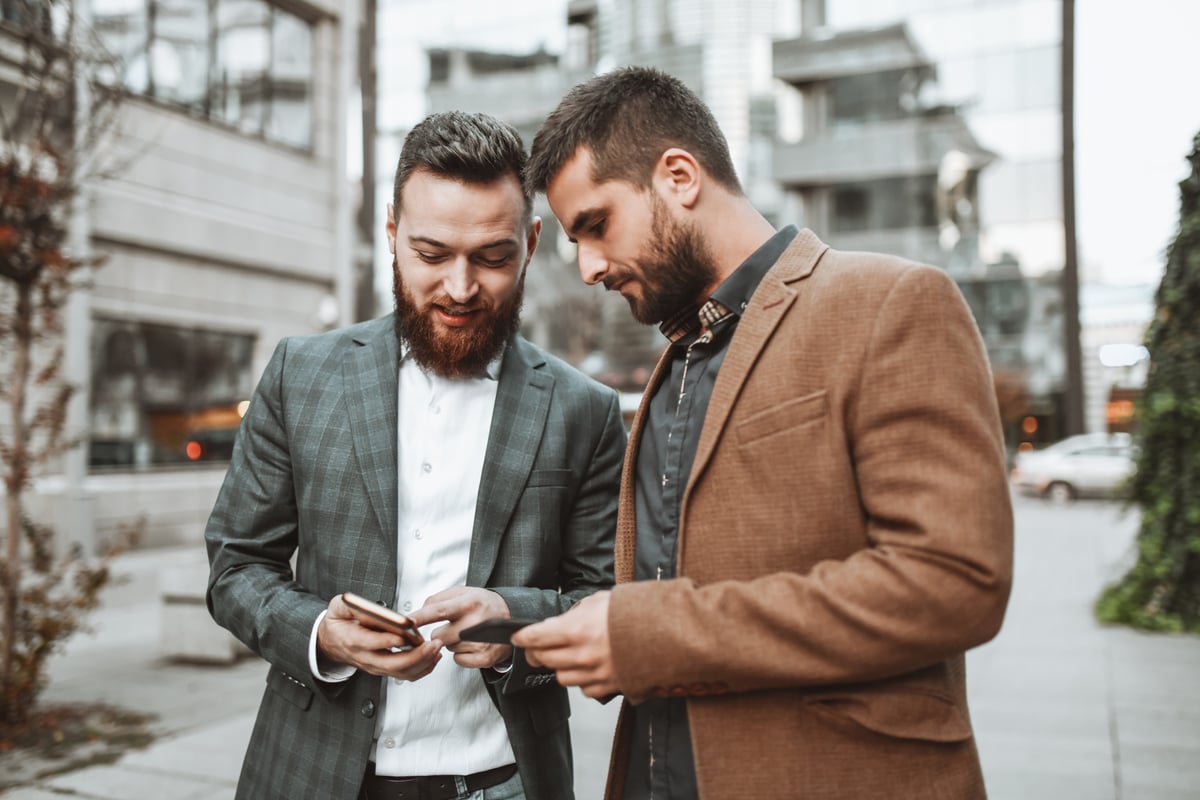 Two investors look at something on a smartphone while outdoors.