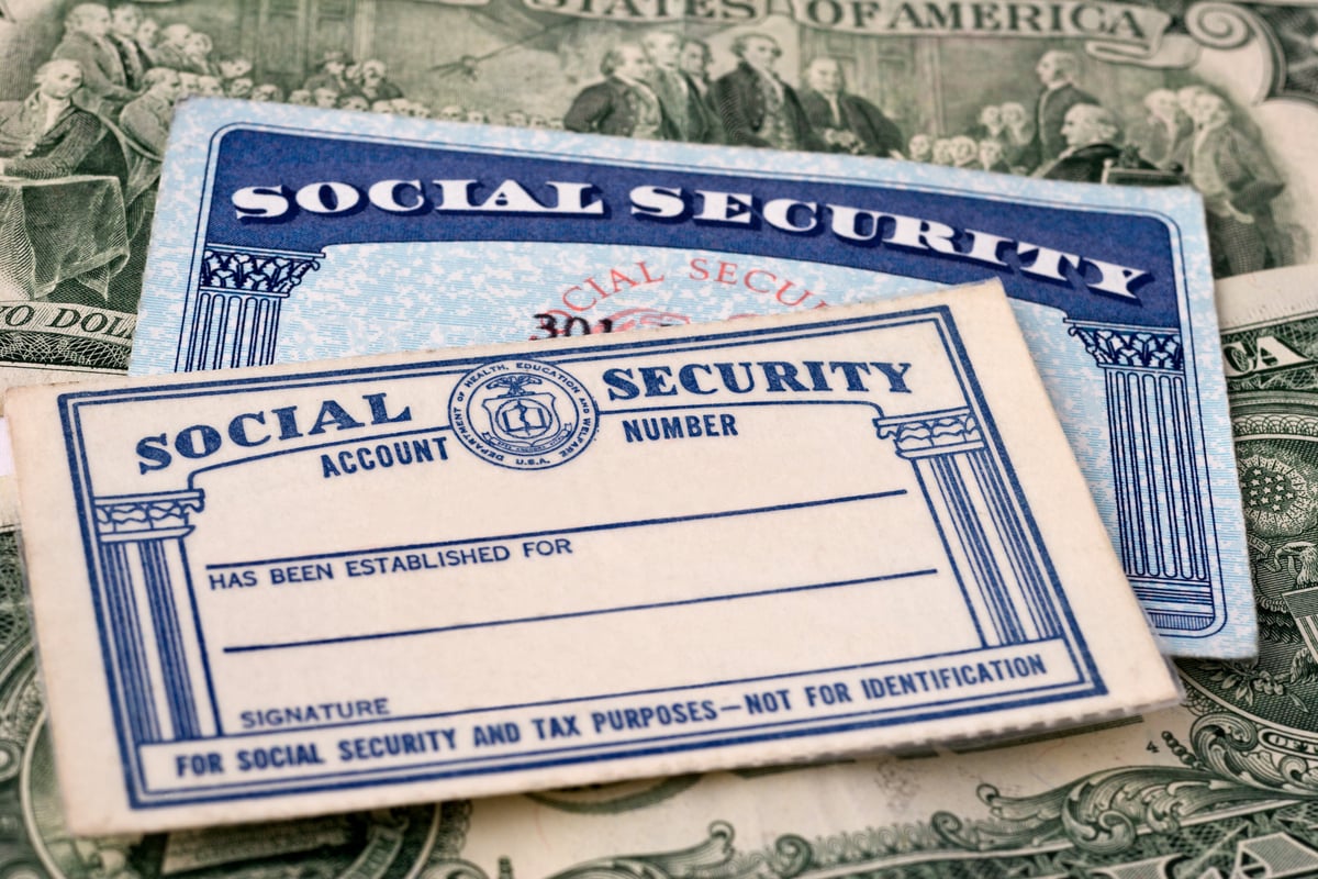 Two Social Security cards (one older) atop a stack of U.S. paper currency.