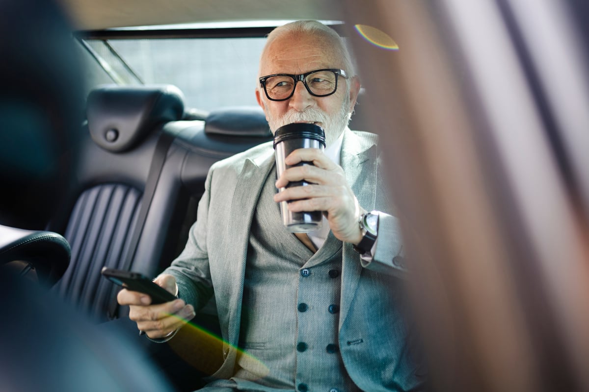 An older person in a car drinking.