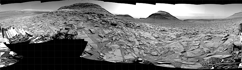 Black and white panorama of rocky desert terrain with hills and buttes in the distance.