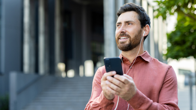 A man swearing wired headphones holding up his phone