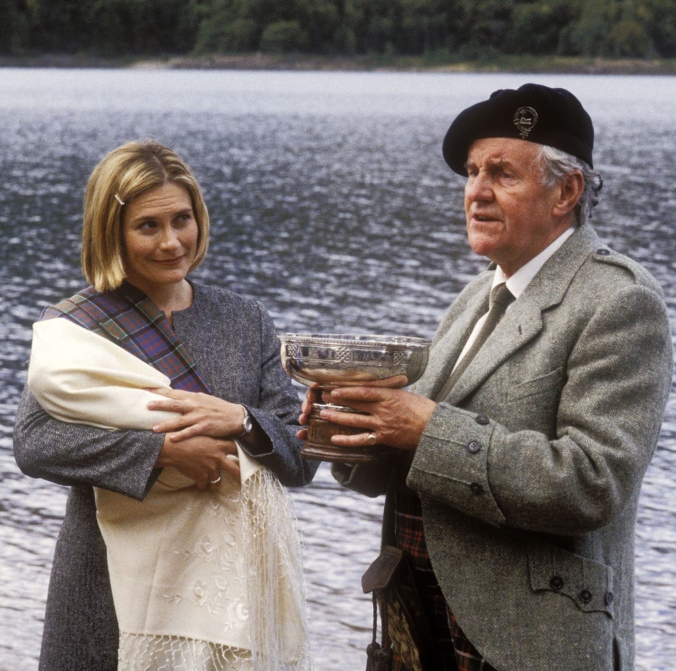 two individuals by a body of water one holding a trophy