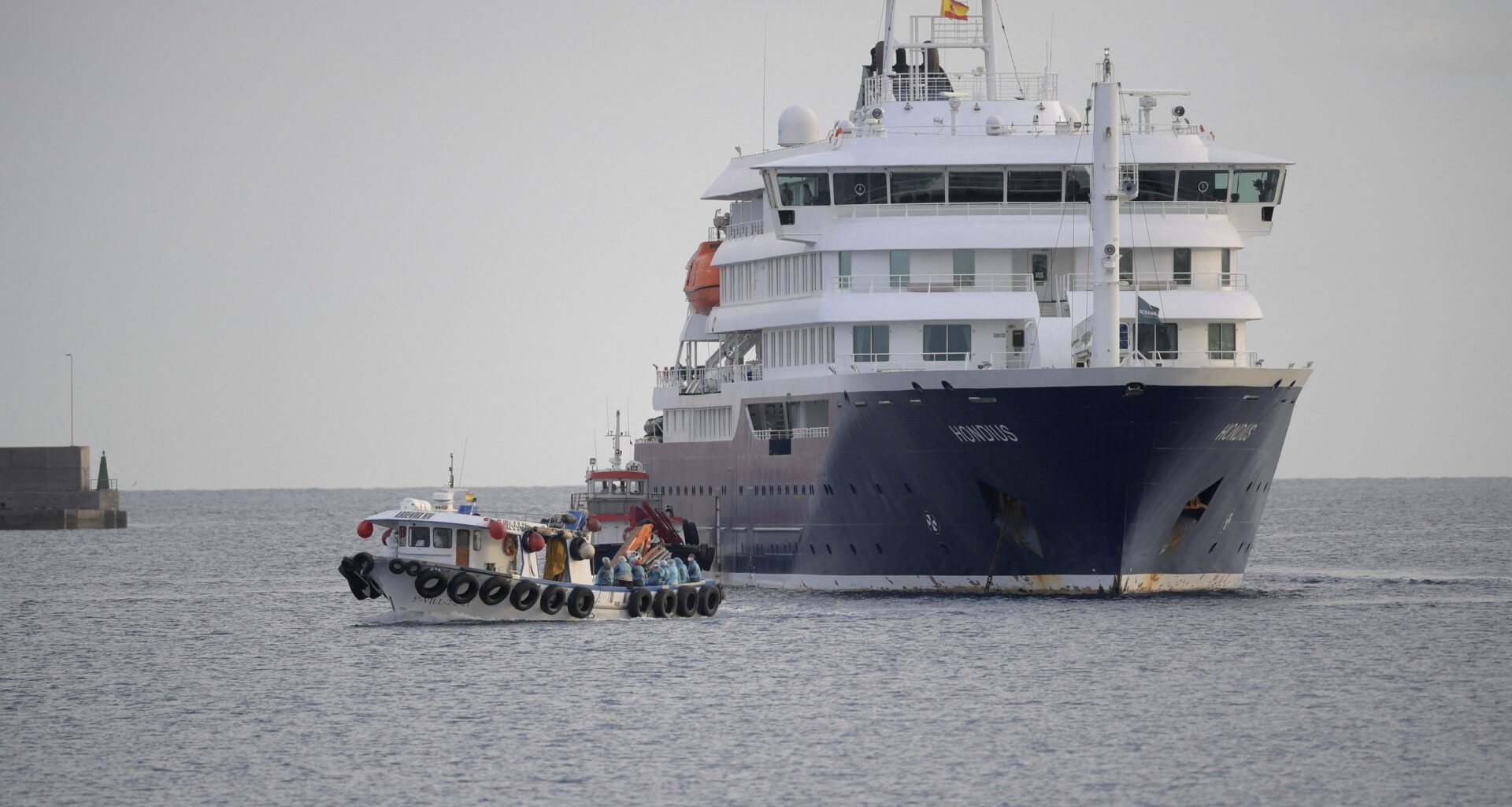 A small boat travels away from the side of a large cruise ship in open water.