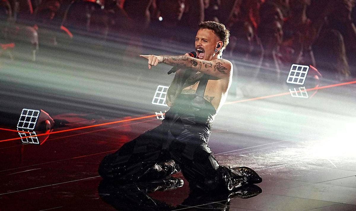 A man kneels on stage as he sings
