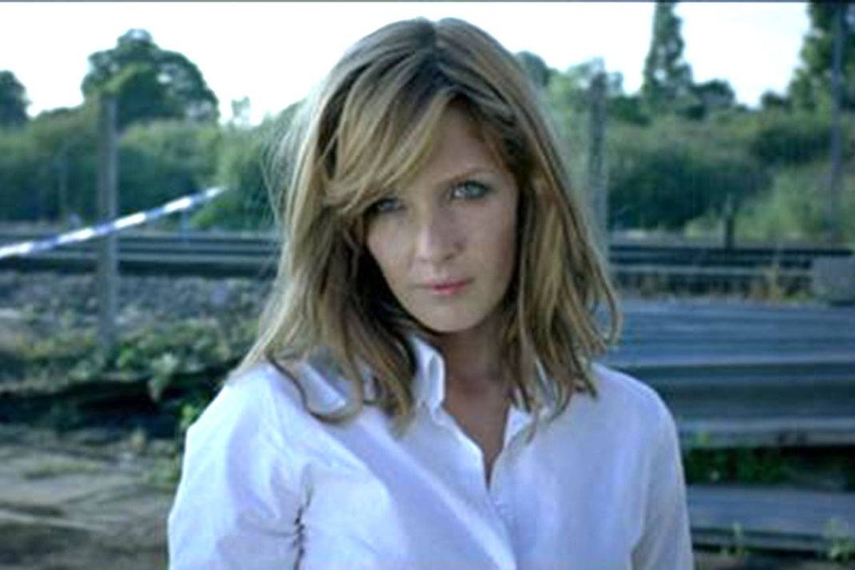 A woman in a white shirt stands in front of police tape