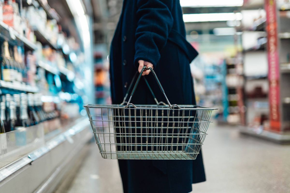 young woman carrying shopping basket, standing at produce aisle in supermarket.