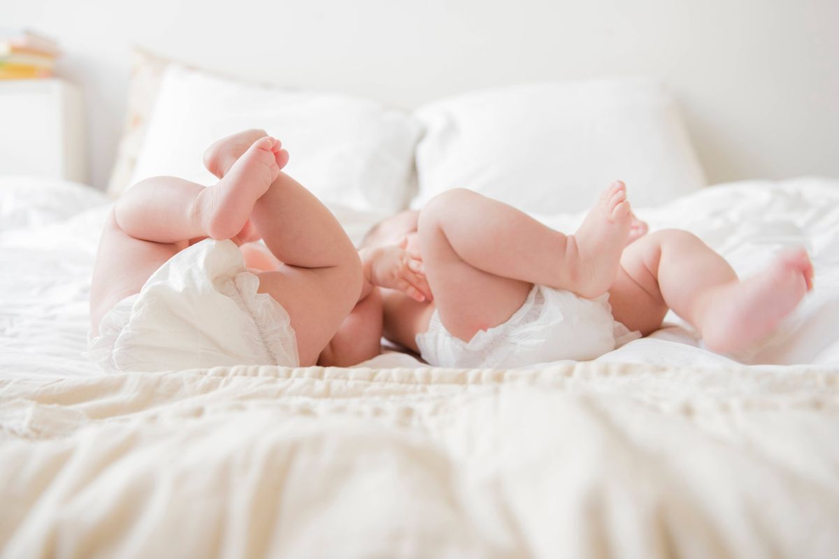 Baby twin girls' legs as they lay on a bed, each wearing nappies.