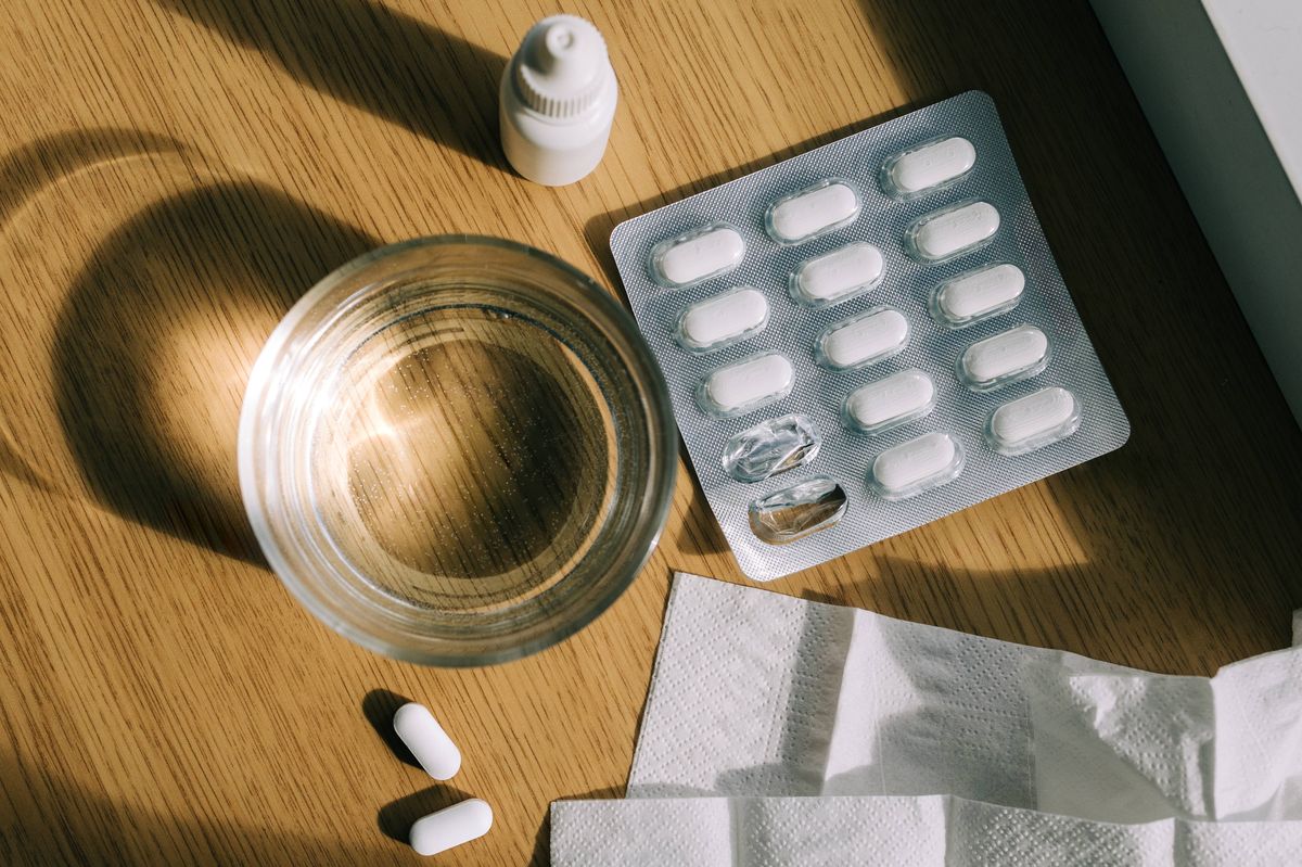 Pills, nasal spray, tissues and glass of water illuminating by sunlight