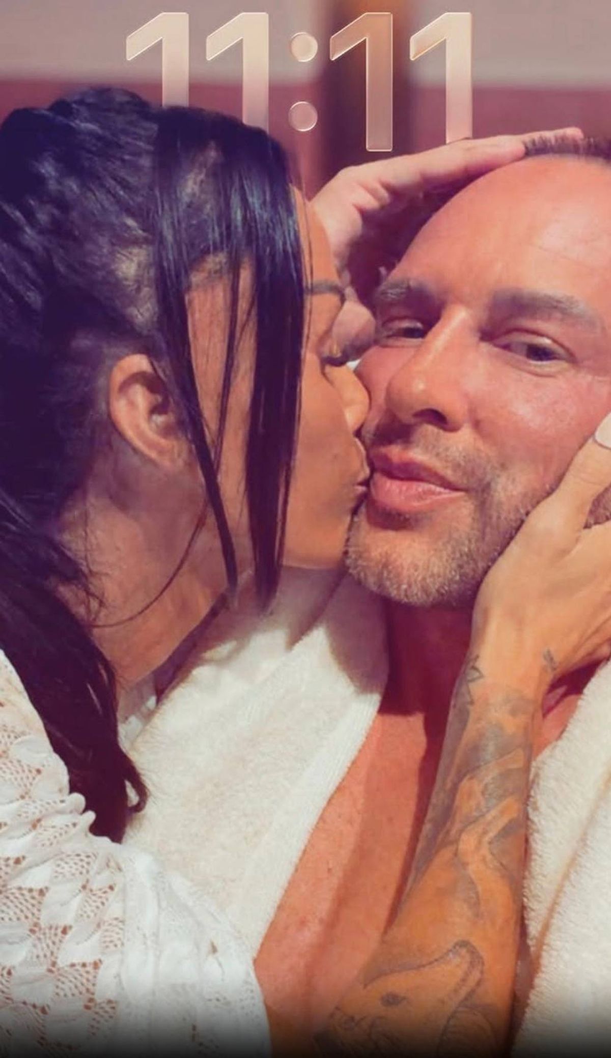 An individual with visible tattoos on their arm is seen in close proximity to another person, both of whom are adorned with white fabric. The image is captured from a low angle, focusing on the intricate details of the tattoos and the soft texture of the white garments.