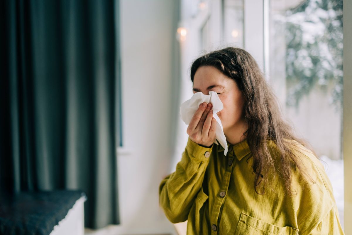 Sick woman blowing her nose with tissue paper at home, suffering from allergy or flu