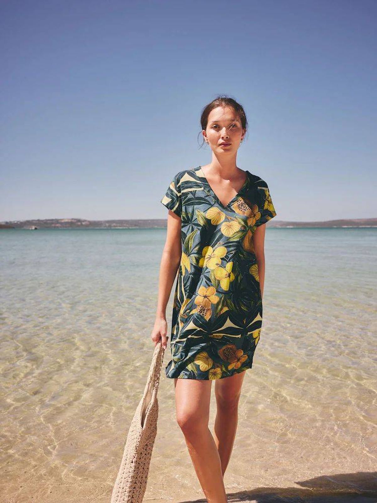 Next Cotton Cap Sleeve V-Neck Mini Dress in navy with a yellow floral print, pictured on a model standing on the beach.