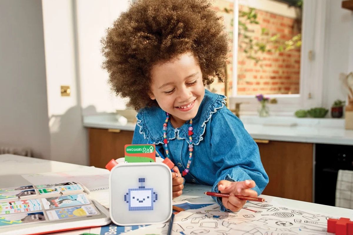 Child with brown curly hair drawing while listening to a Yoto Player