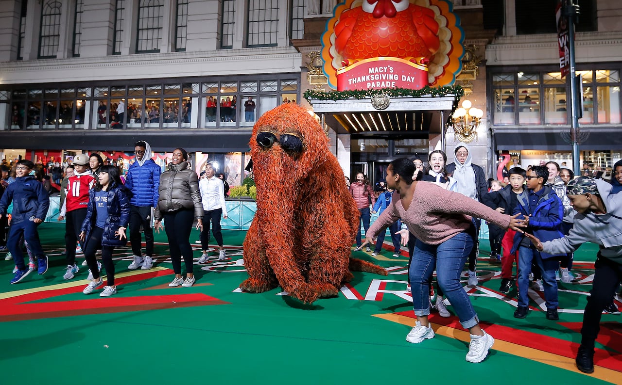 A large shaggy brown muppet surrounded by dancers