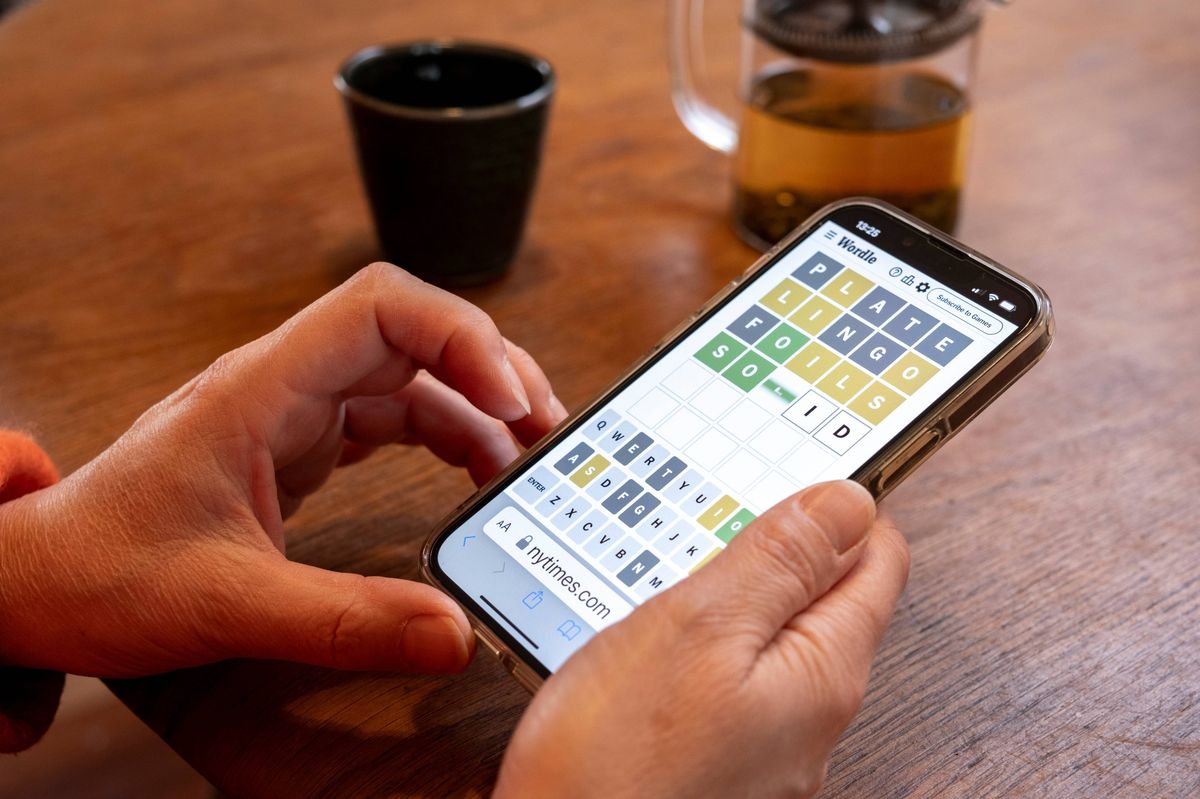 Woman plays Wordle on her smartphone at the kitchen table 