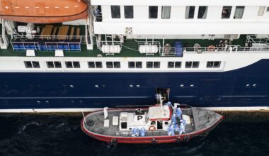 People in blue hazmat suits are on a small boat running alongside a cruise ship.