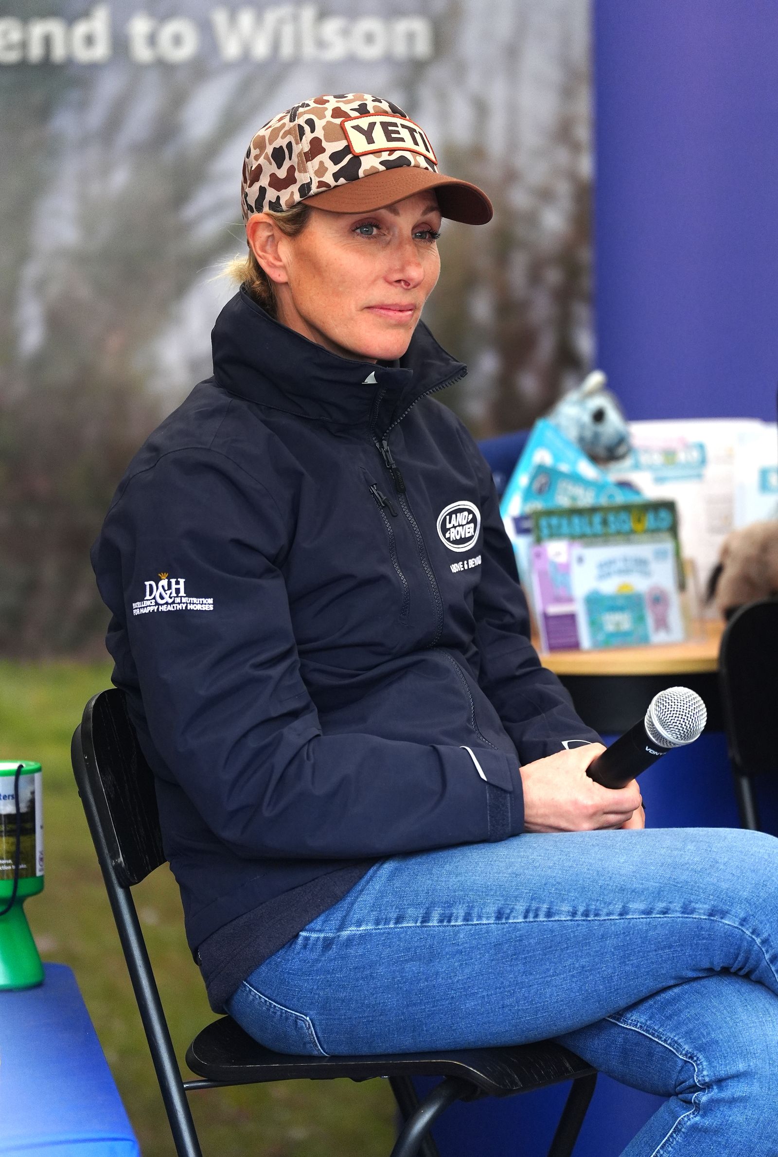 Image may contain Zara Tindall Baseball Cap Cap Clothing Hat Person Sitting Coat Electrical Device and Microphone