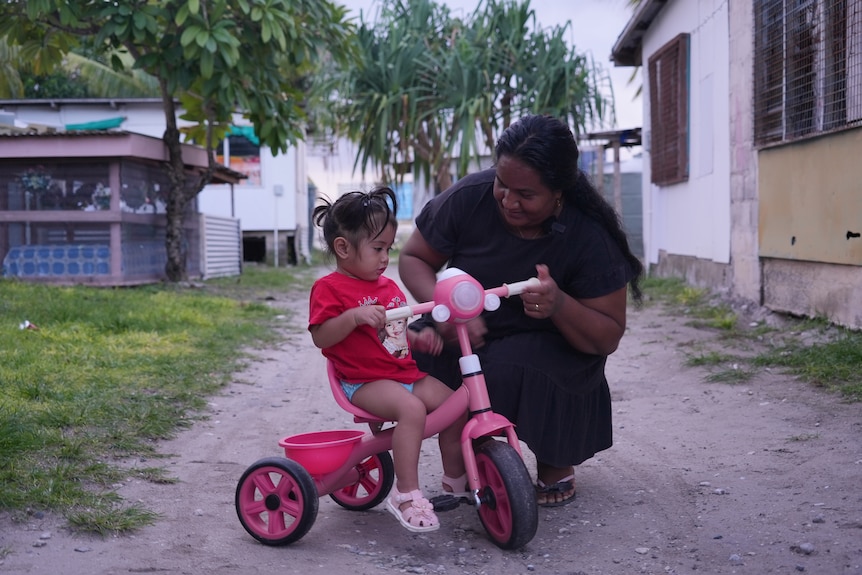 A photo of Stella kneeling next to her daughter on a bike.