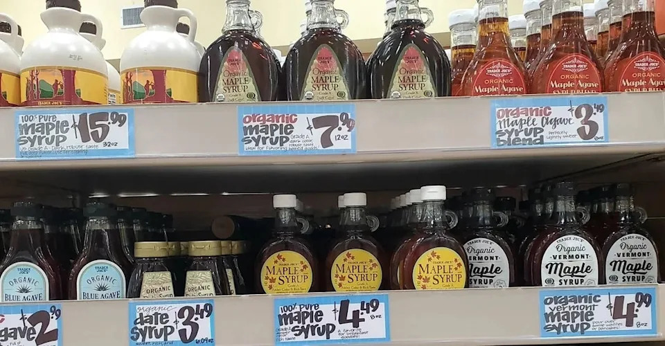 Various maple syrup bottles displayed on a store shelf, each with different prices and labels, including organic and Vermont options