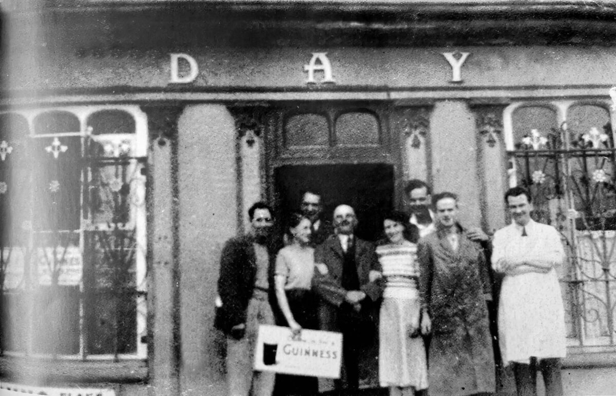 A group of people outside Day’s pub in Whitegate with proprietor William Day centre with moustache. Kevin Day is in the white coat, his son, a butcher, with Day employee Davy Ryan beside him. Picture supplied by Micheál Kenefick