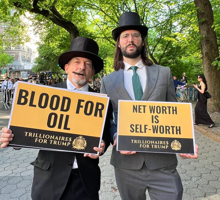 Protesters Andrew Boyd (left) and Schuyler deVos (right) mock Jeff Bezos and his billionaire friends by holding signs that read "BLOOD FOR OIL" and "NET WORTH IS SELF-WORTH" along with the shared message "TRILLIONAIRES FOR TRUMP" outside the Met Gala.
