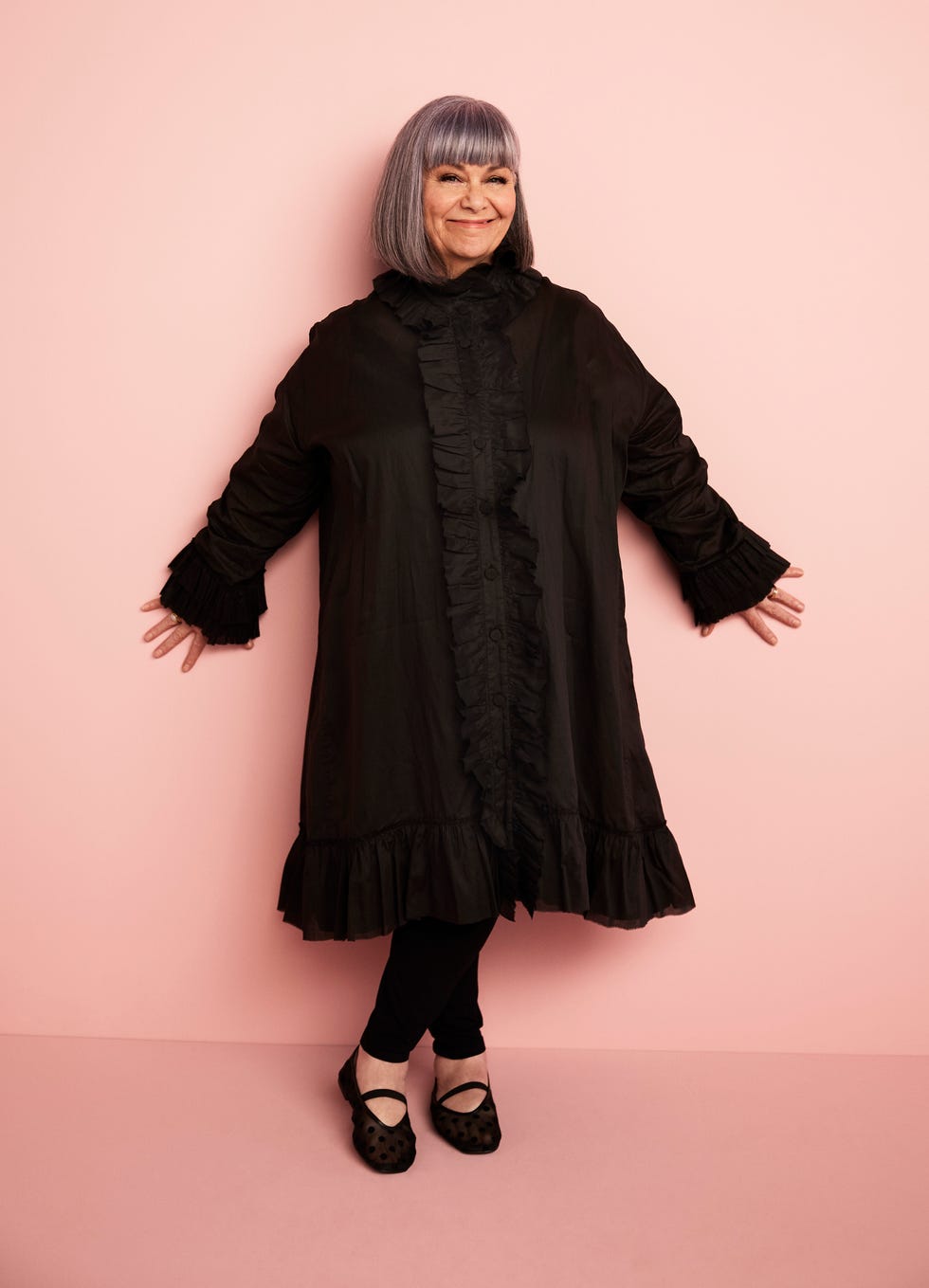 individual in a black ruffled coat with a light pink background individual in a black ruffled coat with a light pink background