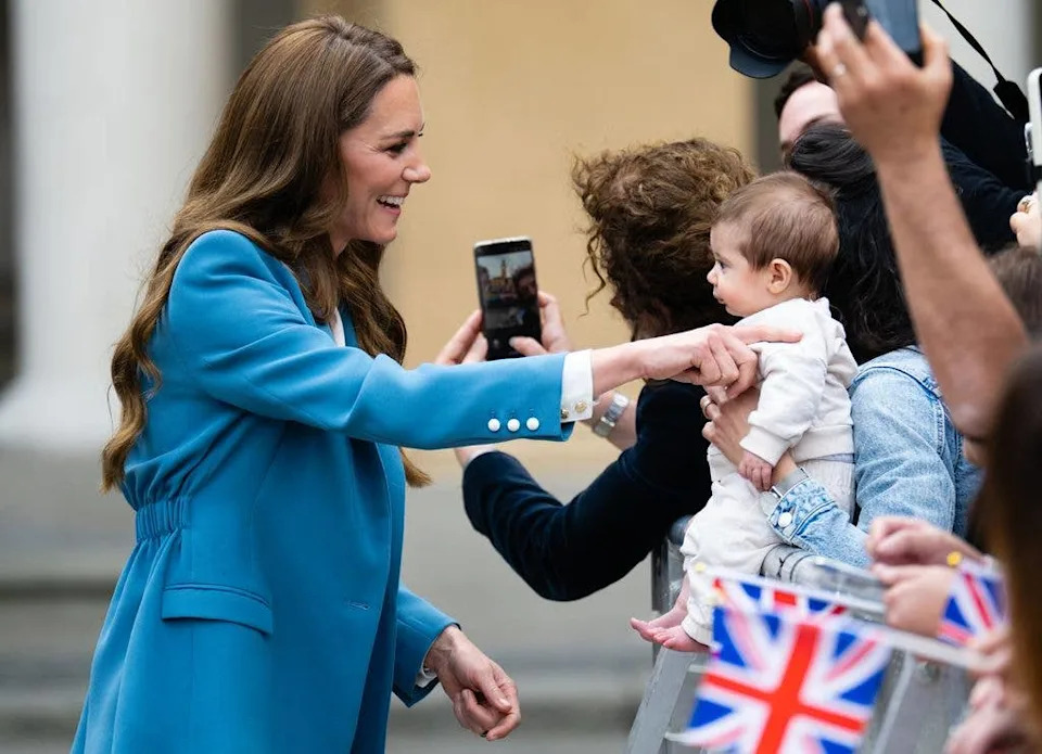 Catherine, Princess of Wales greets a baby in the crowd as she visits the Piazza Camillo Prampolini 