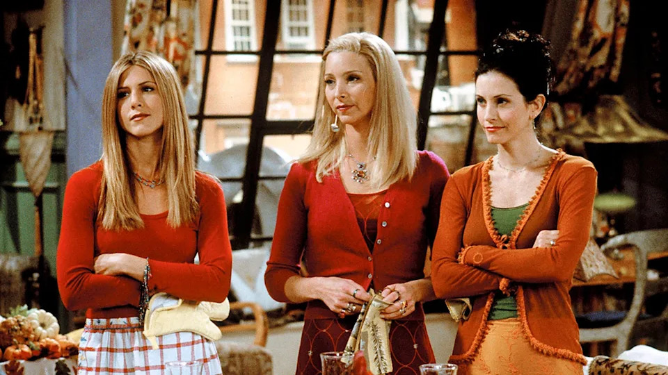 Jennifer Aniston and Lisa Kudrow in red as Rachel and Phoebe on 'Friends' standing next to Courteney Cox as Monica in orange, all looking unamused