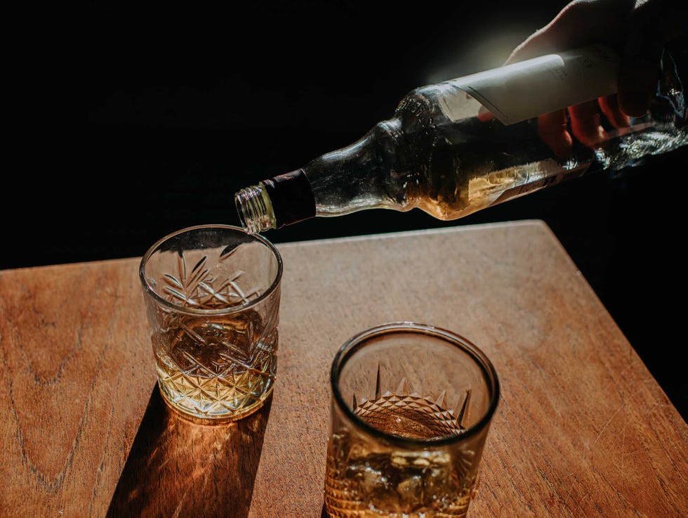 a bottle of whisky is poured into a cut glass tumbler over ice space for copy