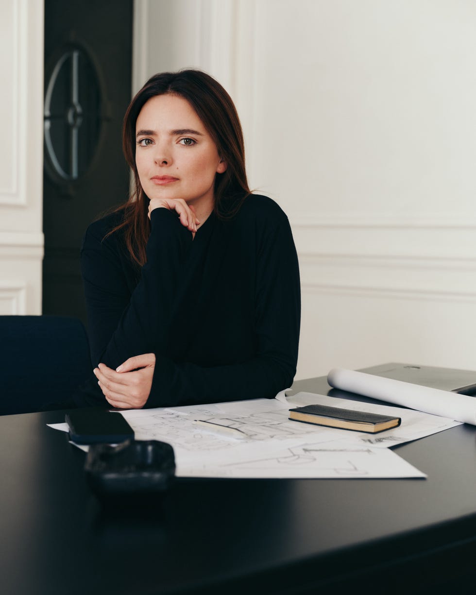 Woman seated at a desk with architectural plans and a notebook.