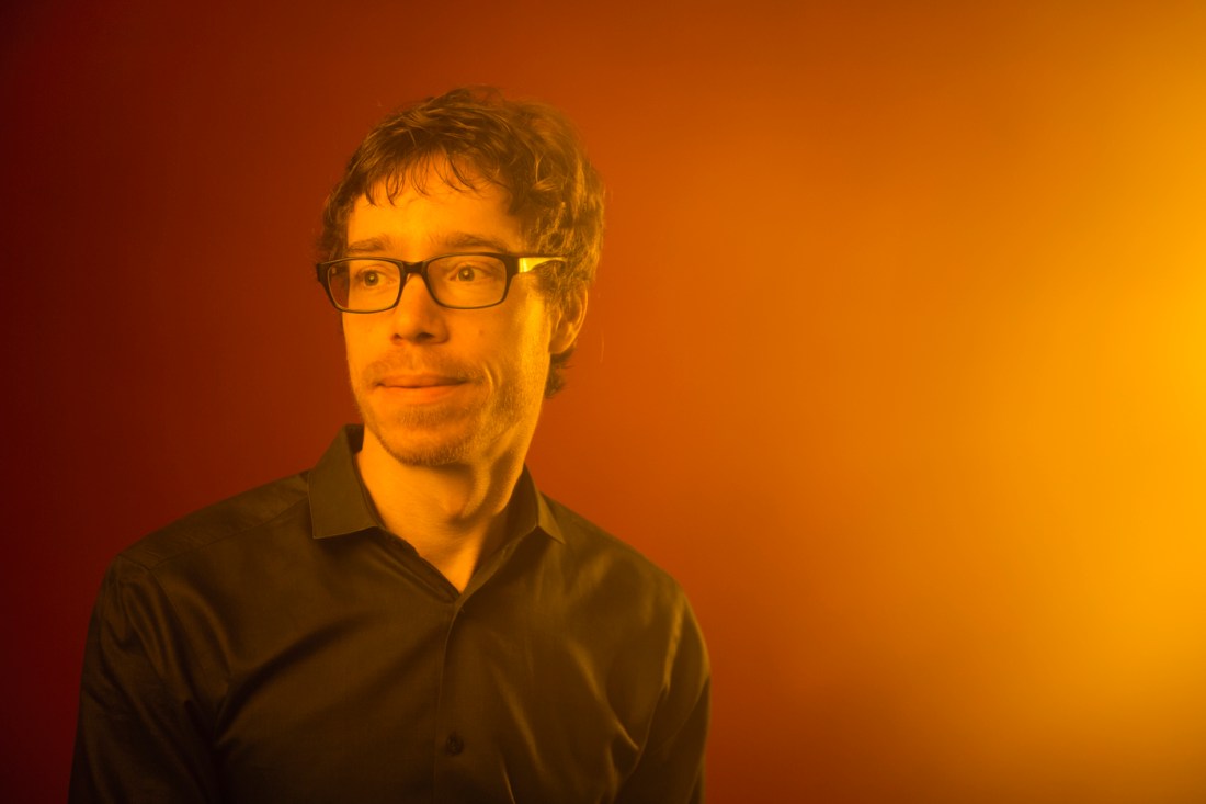 Christoph Riedl, Northeastern professor of computer science, information systems, and network science, posing for a portrait against a warm orange-toned background. 