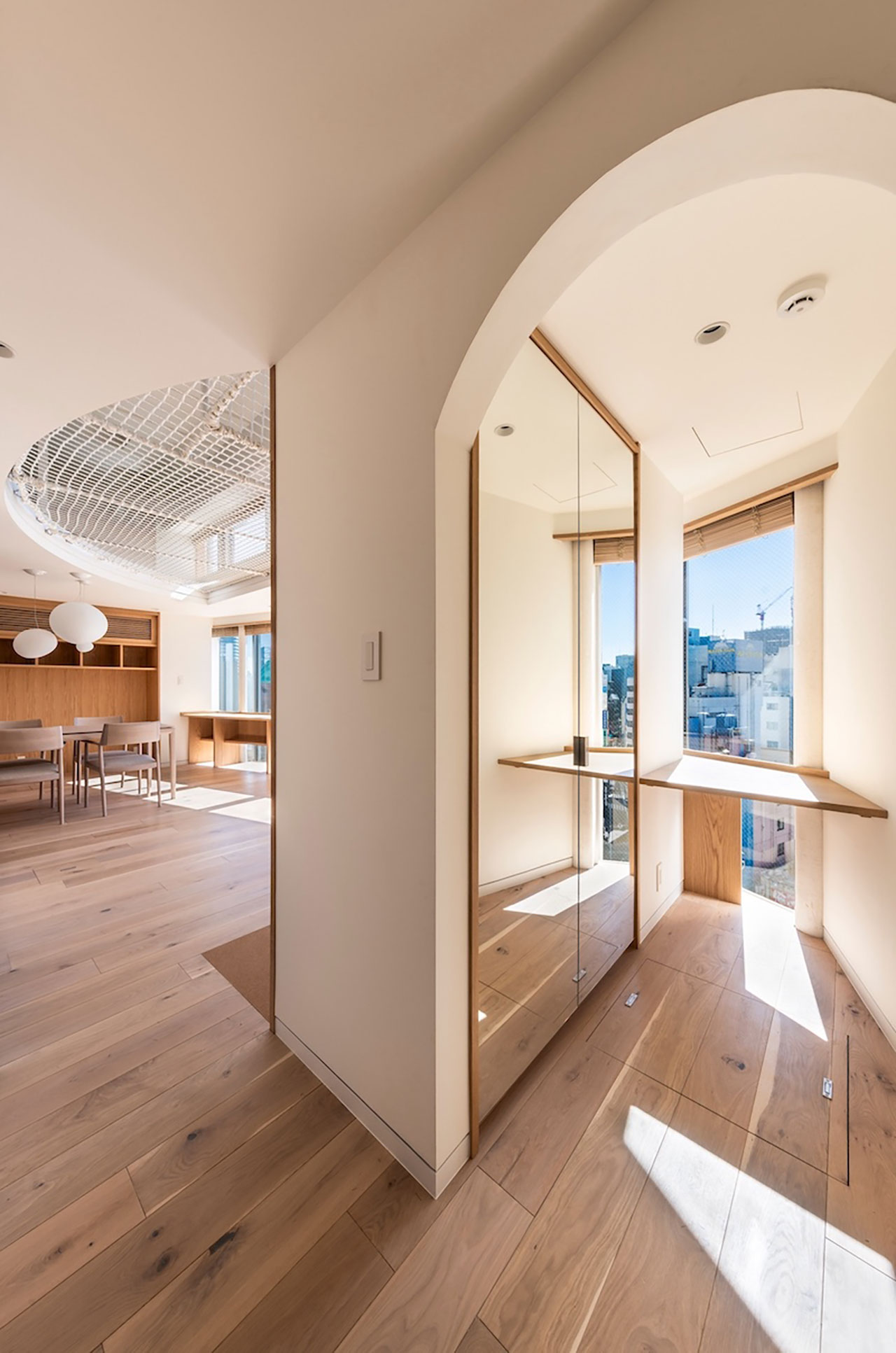 Modern apartment interior with wooden floors, large windows, built-in mirrors, archway, and open dining area with ample natural light.